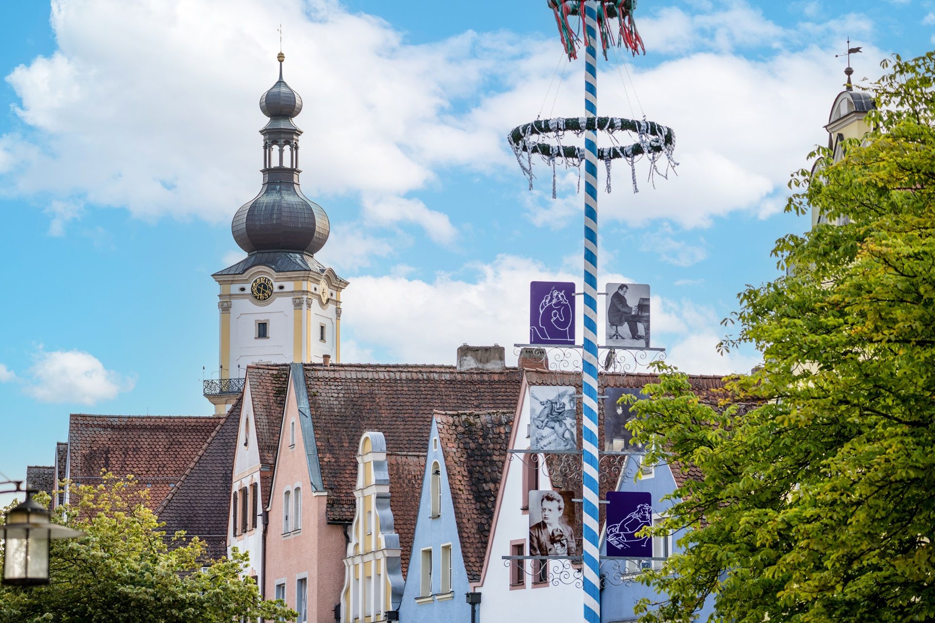 Auf dem Bild sind die Weidener Altstadthäuser und ein Maibaum im Vordergrund zu sehen. Im Hintergrund ist der Kirchturm St. Michael zu sehen.